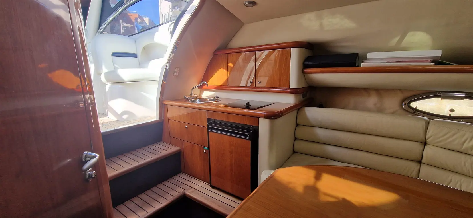 Interior view of a yacht with a kitchenette, wooden cabinetry, a dining table, and steps leading to an upper deck.